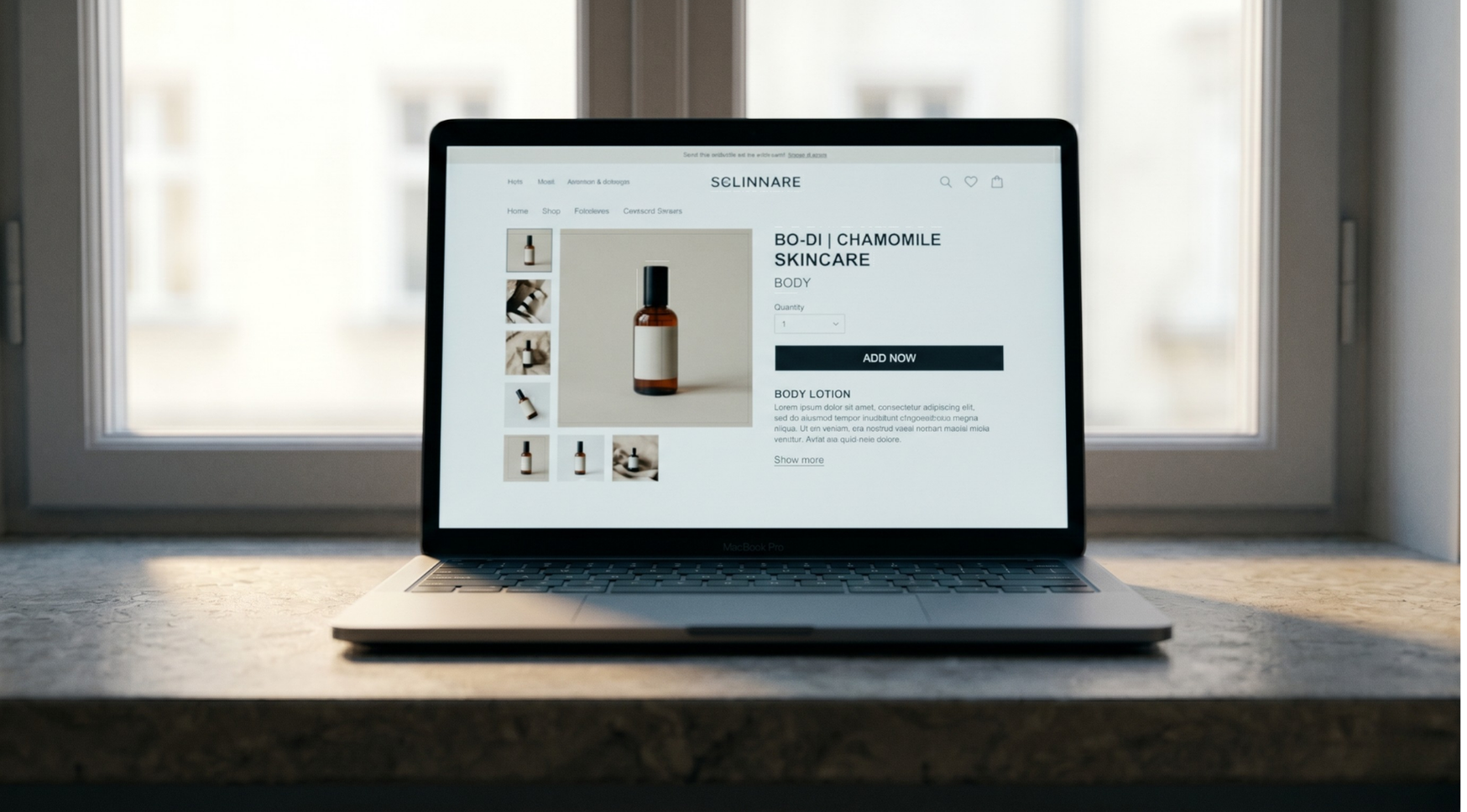 A laptop on a stone counter by a window — the screen shows a minimalist skincare ecommerce product page in soft natural light.